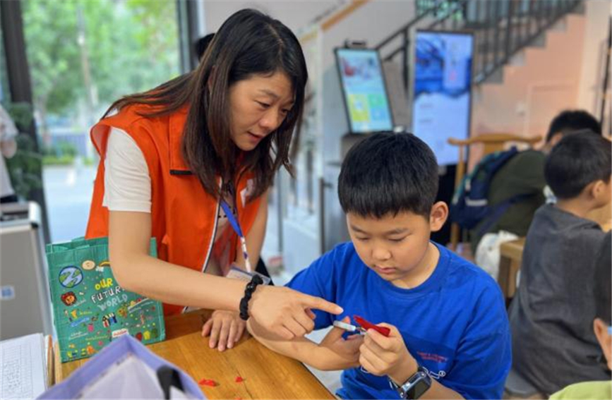 7月18日，志愿者在西安市未央区中海开元壹号社区的托管班上指导孩子学习剪纸。未央区委宣传部供图